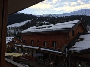 A wooden building with a snow-covered roof, a balcony, and a view of a snowy mountain range. - Apartment/ flat - Meribel (Les Allues)