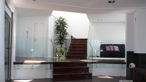 Ein modernes Interieur mit Treppe, Glasgeländern, einer Topfpflanze und einem Bett mit Kissen.