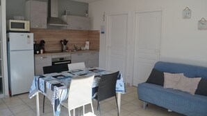 Une cuisine compacte équipée d’un four à micro-ondes, d’un réfrigérateur et d’une cuisinière. On y trouve une table à manger avec des chaises, ainsi qu’un canapé bleu dans l’espace salon.
