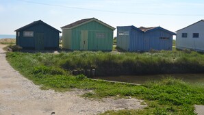 Une rangée de petits bâtiments à un seul étage, avec un chemin de terre menant à un canal.