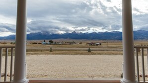 A view from a porch with white columns, overlooking a rural landscape with mountains and scattered houses. - Lamp Post Lodge (Westcliffe)