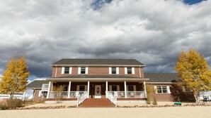 A two-story brick house with a front porch, a driveway, and a gravel lawn. - Lamp Post Lodge (Westcliffe)
