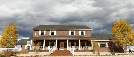 A two-story brick house with a front porch, a driveway, and a gravel lawn.