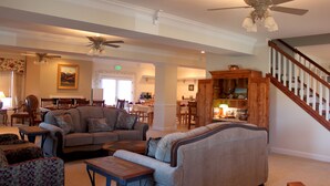 A spacious living room with a large sofa, a coffee table, and a dining area in the background. There is a wooden staircase leading to another level. - Lamp Post Lodge (Westcliffe)