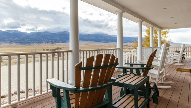 A covered porch with Adirondack chairs and a view of mountains. - Lamp Post Lodge (Westcliffe)