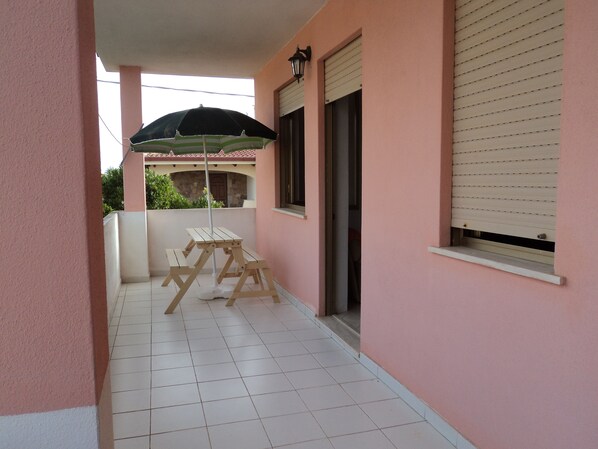 Un espacio al aire libre cubierto con una mesa de picnic y una sombrilla, suelo de baldosas y pared rosa.