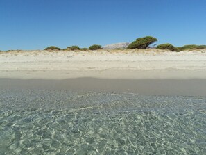 Una playa con aguas transparentes y poco profundas, y dunas a lo lejos.