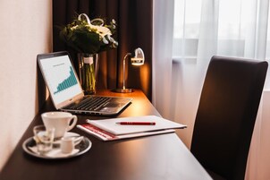 Una laptop mostrando un gráfico, una taza de café, un florero con flores y una lámpara de escritorio sobre una mesa de madera.