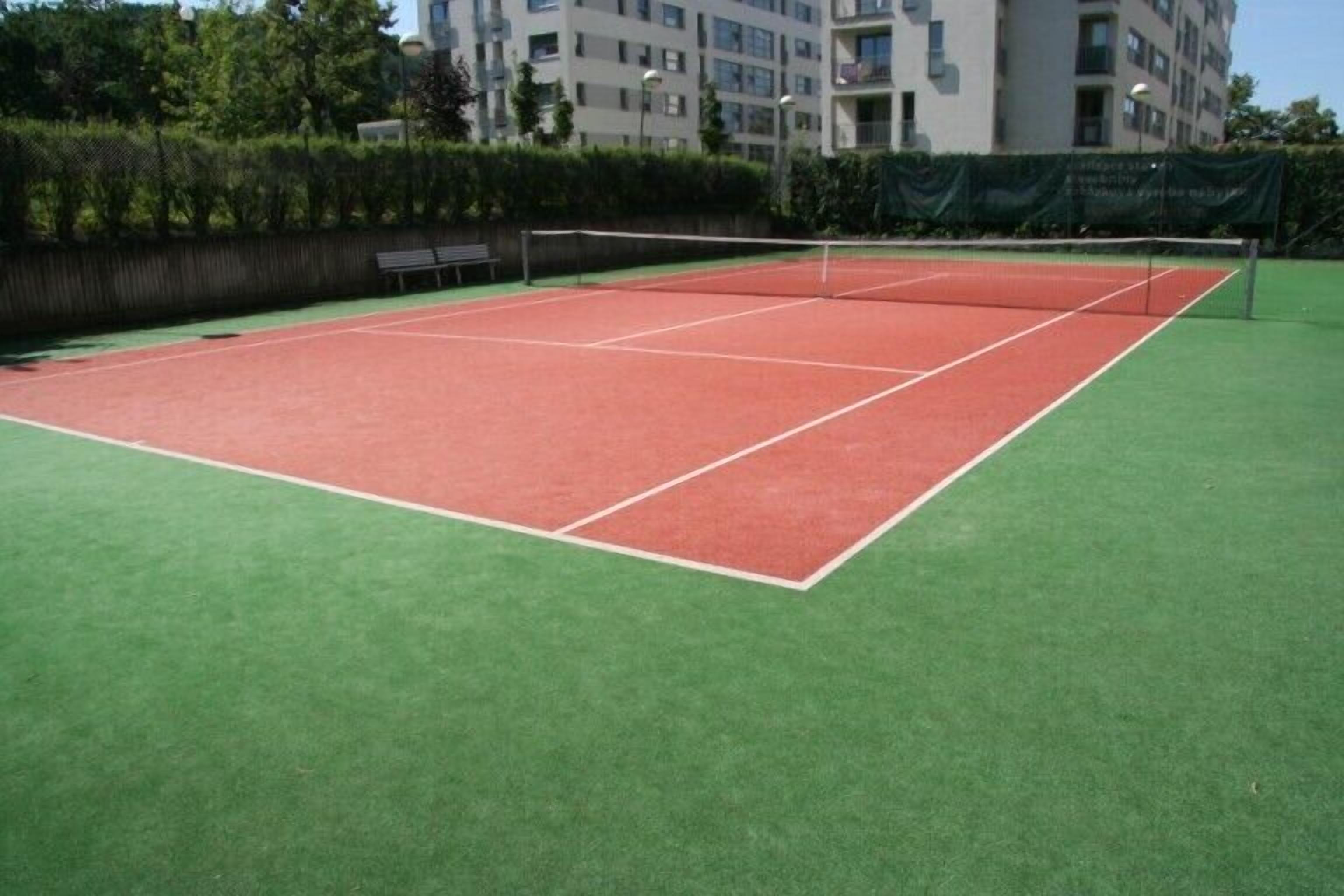 Een tennisbaan met een net in het midden, omgeven door een groene ondergrond.