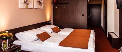 A hotel room with a large bed, a nightstand with a vase of flowers, and artwork on the wall.