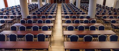 A conference room with rows of tables and chairs, large windows, and a central aisle.