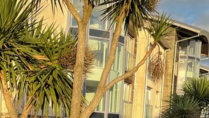 A stone sign with "OCANI" engraved, surrounded by tropical plants and a modern building with large windows. - Magnificent Sea views, Central, 2 double bedrooms, 2 bathroom. Pets welcome.   (Newquay)
