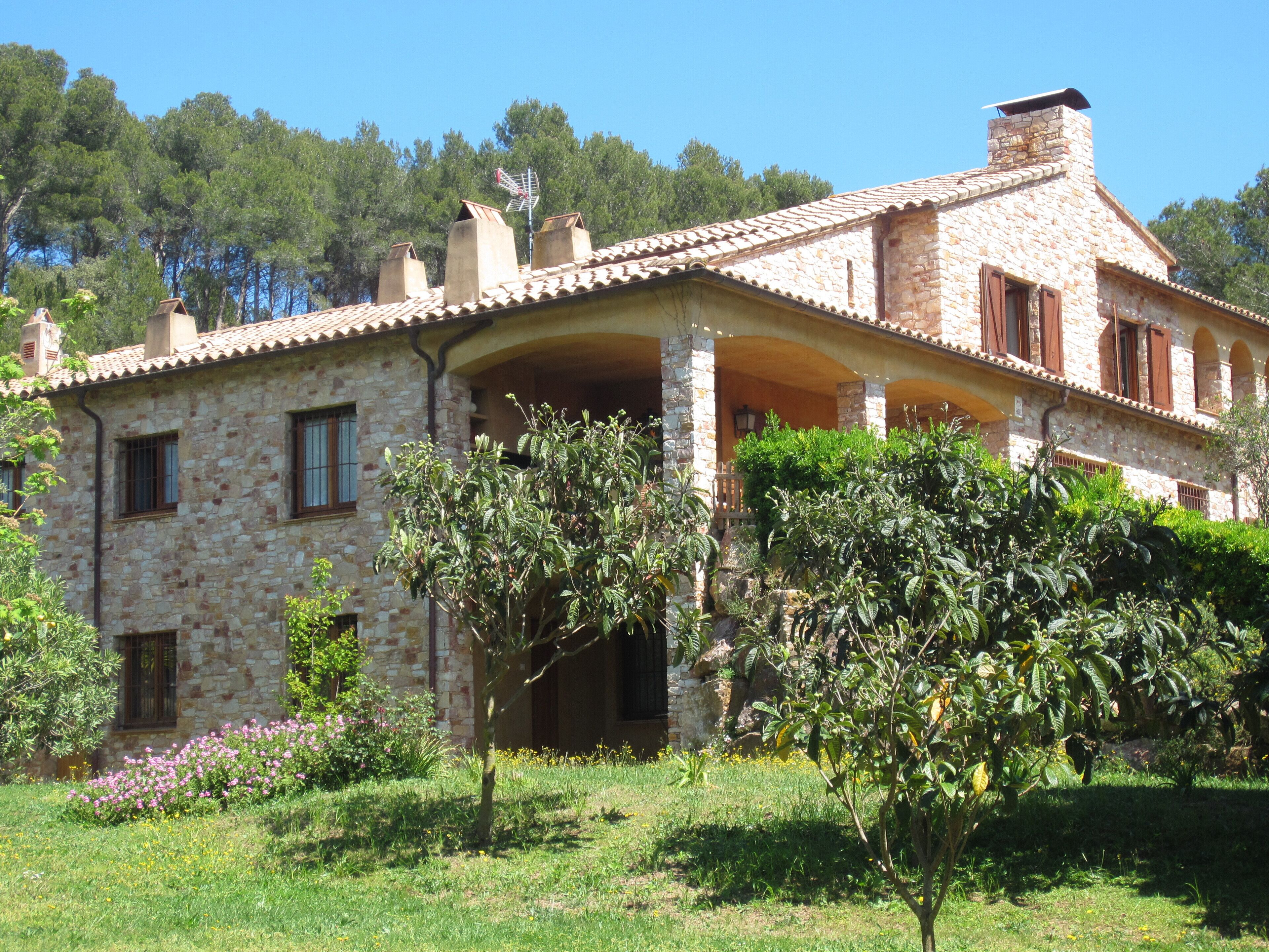 Une maison en pierre avec un toit en tuiles, plusieurs cheminées et un porche abrité.