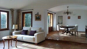 Een woonkamer met een bank, een klein tafeltje, een eettafel met stoelen en een kroonluchter.