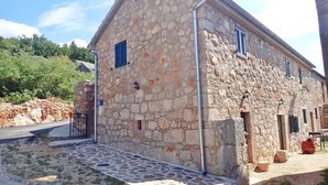 A stone building with a sloped roof, a gated entrance, and a paved area with a wooden log. - Mareta apartment with free wifi in a stone house (Seline)