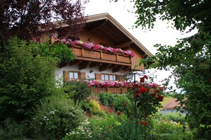 A traditional chalet with a wooden balcony adorned with flowers, surrounded by lush greenery. - Holiday home in quiet location with terace and panoramic view (Regen)