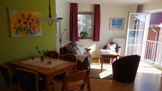 Ett mysigt vardagsrum med ett matbord, en soffa och stolar. Det finns ett fönster med gardiner, en lampa och en tavla på väggen.
