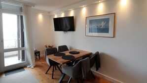 Un comedor con una mesa de madera, sillas, un televisor montado en la pared y un cuadro enmarcado.