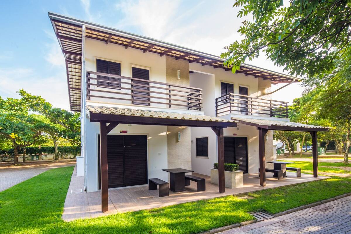 Una casa de dos pisos con un porche cubierto, un balcón y un pequeño jardín.