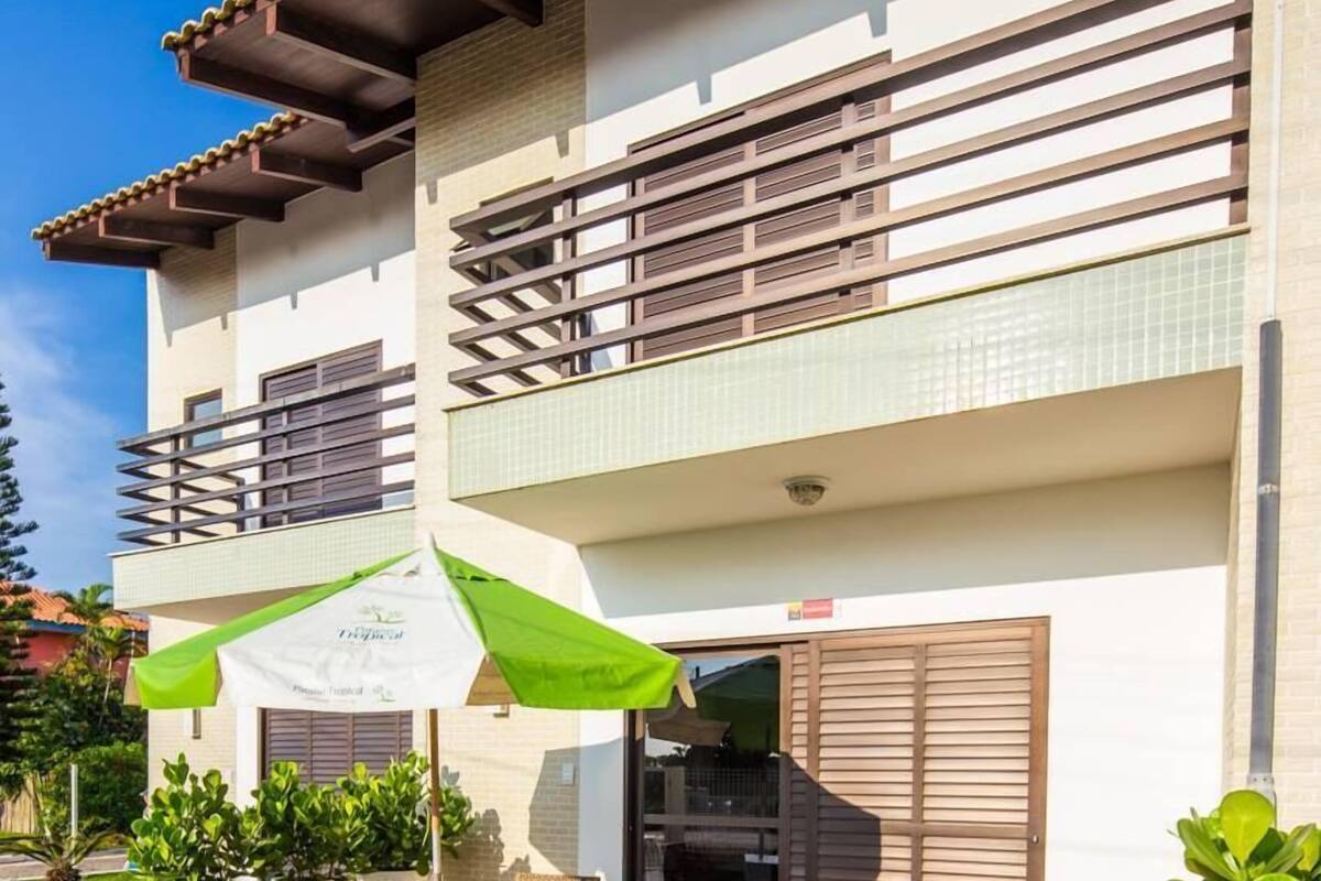 Edificio de dos pisos con un patio que tiene mesa y sillas, una parrilla y plantas en macetas.