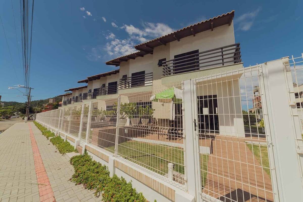 Un edificio residencial con varios balcones, un camino pavimentado y un área cercada con mobiliario exterior.