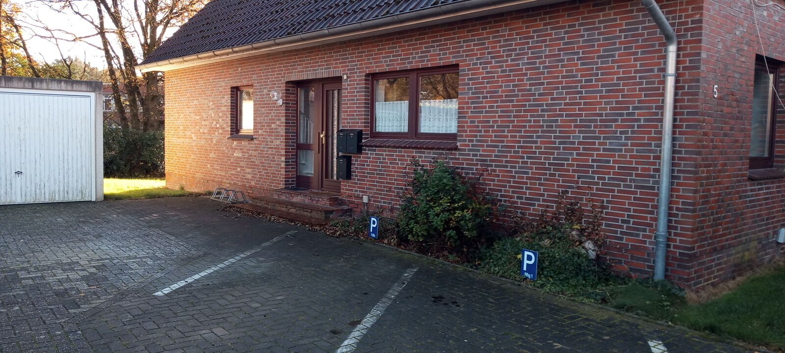 A brick building with a garage, a small garden, and a parking area.