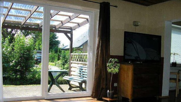 A room with a wooden floor, a table, a bench, a potted plant, and a TV.