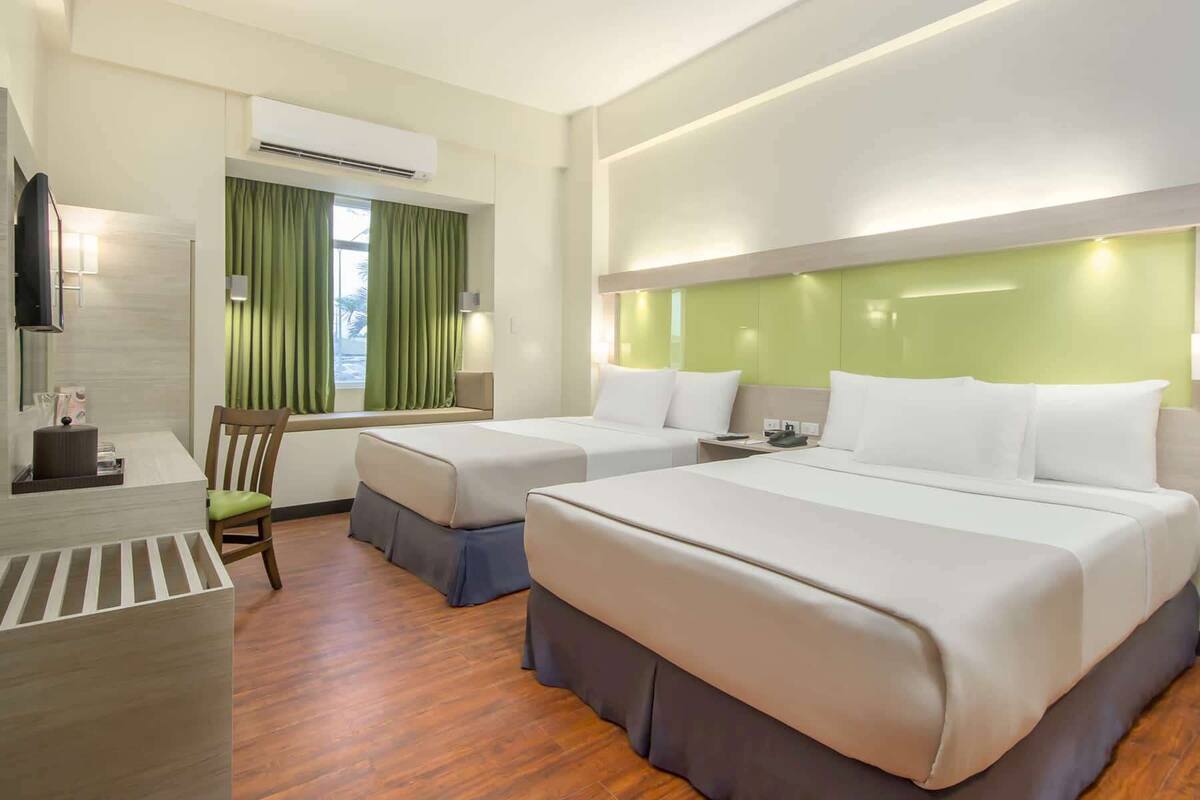 A hotel room with two beds, a desk, a chair, and a window with curtains.