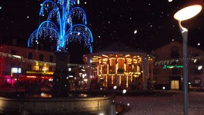 Una piazza con una fontana e strutture illuminate, circondata da edifici con insegne ben visibili.