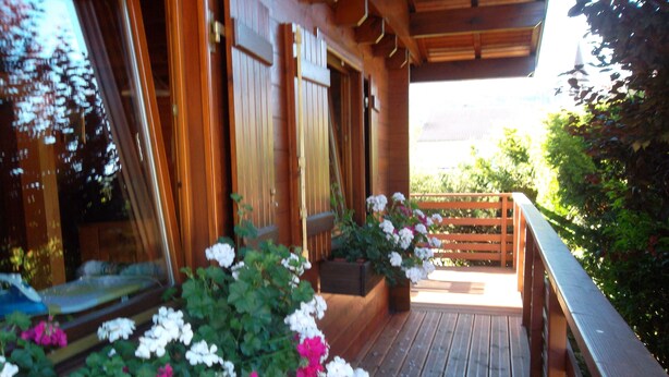 Un patio in legno con ringhiera in legno, circondato da vasi con fiori bianchi e rosa.