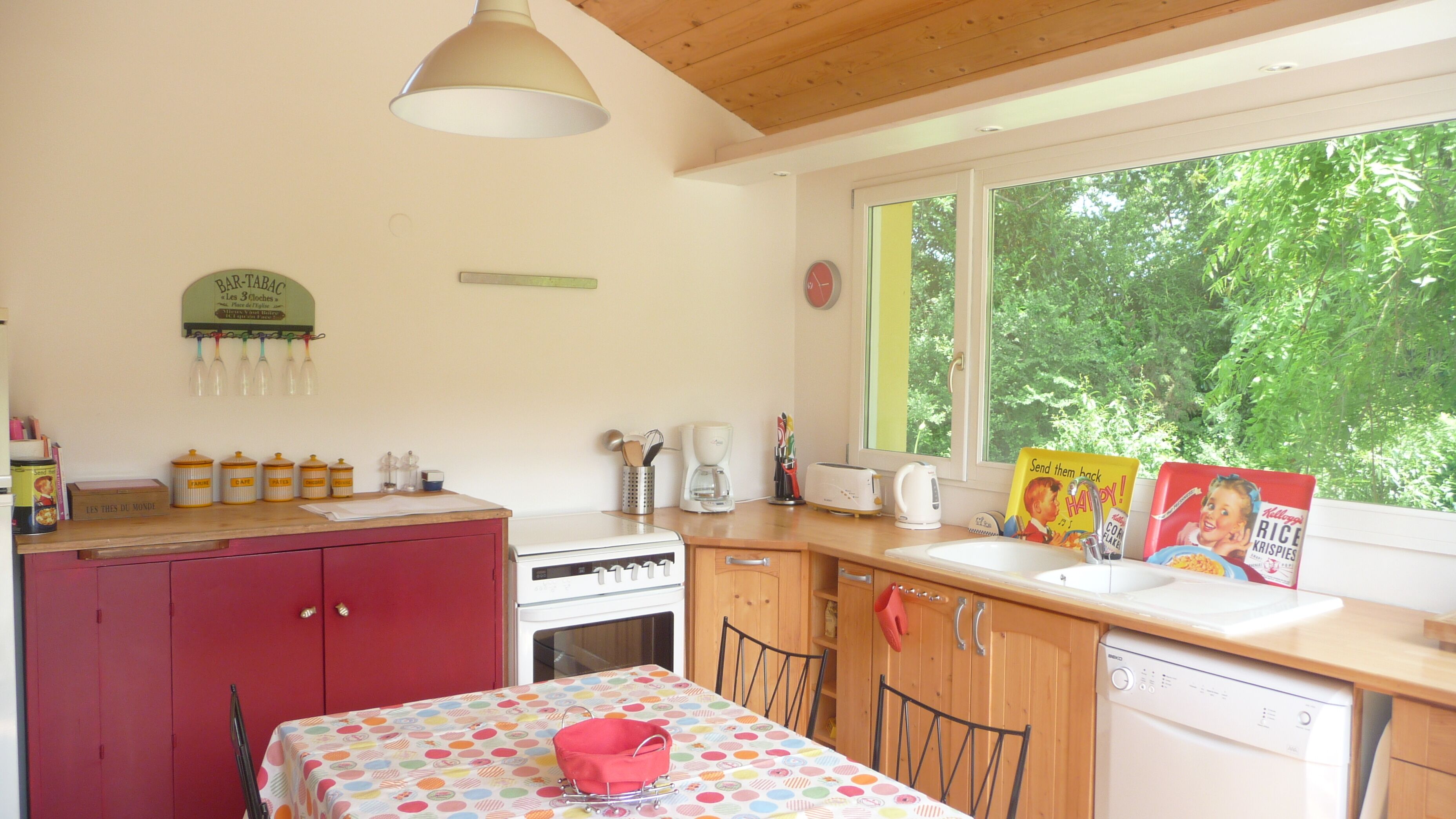 A kitchen with a wooden table, a red cabinet, a white stove, and a window with a view of trees.