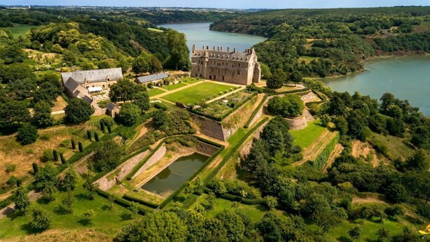 Un grand château doté d’un jardin bien entretenu et d’un lac en arrière-plan.
