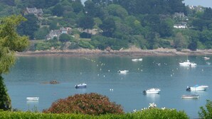 Un paysage côtier avec plusieurs bateaux sur une eau calme, entouré d’une végétation luxuriante et de maisons situées sur une colline.