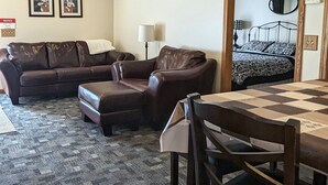 Una habitació amb un sofà de pell marró, una taula petita i un llit amb roba de llit estampada.
