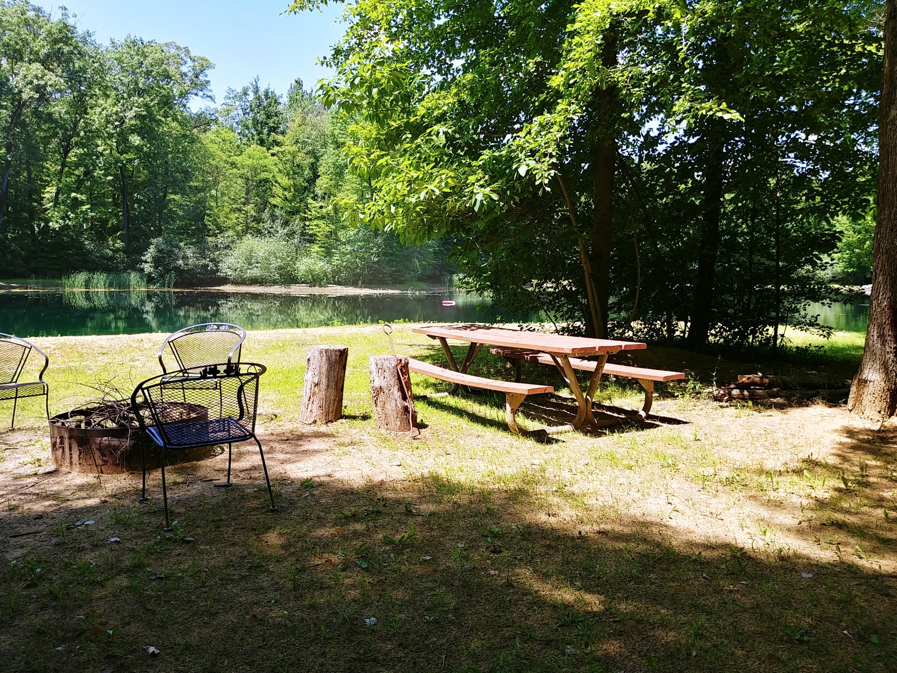 A picnic area with metal chairs, a wooden picnic table, and a fire pit.