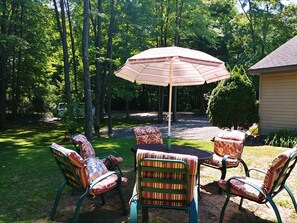 Une terrasse extérieure avec quatre chaises et une table, entourée d’arbres et bordée d’un chemin de gravier.