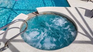 A hot tub with a metal railing, surrounded by a tiled pool area.