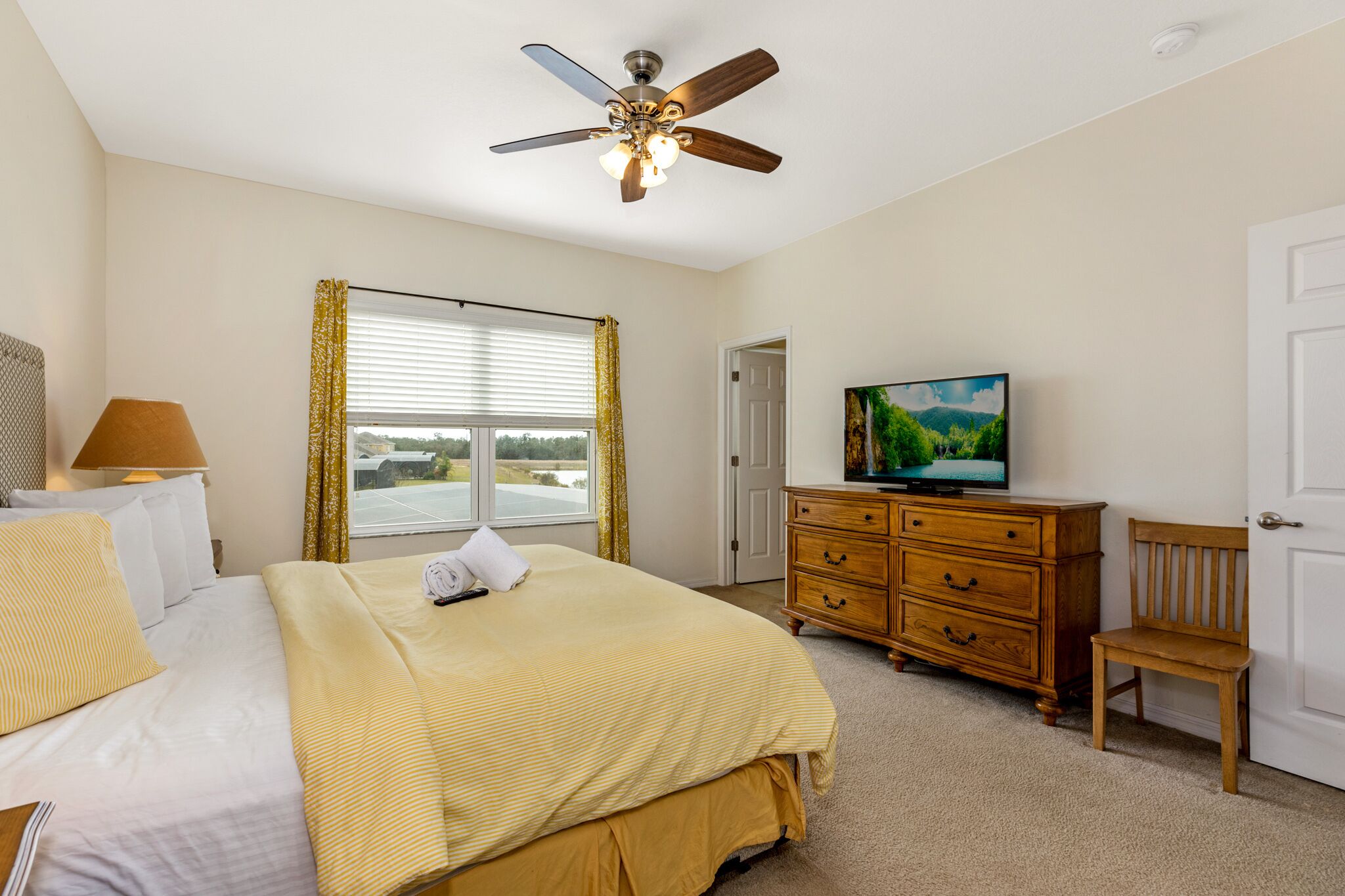 A bedroom with a bed, a dresser, a television, a ceiling fan, and a window with curtains.