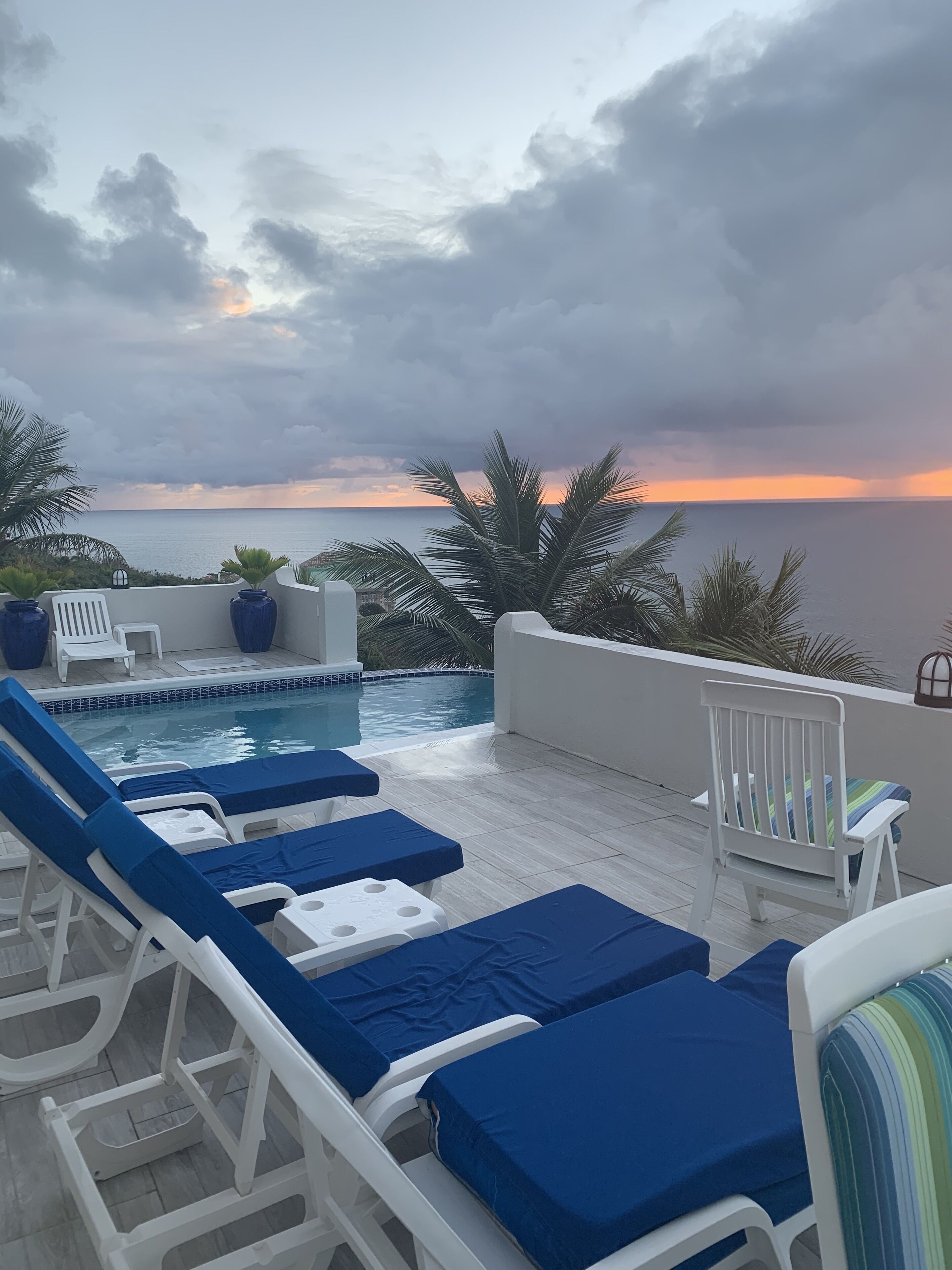 Ein Poolbereich mit Liegestühlen und Blick auf den Sonnenuntergang über dem Meer.