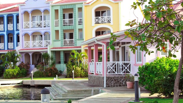 A row of colorful buildings with balconies, a small pond, and a wooden dock.