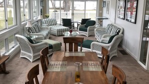 A spacious living room with a wooden dining table, wicker furniture, and large windows offering a view of the outdoors. - Powers Lake spacious retreat (Powers Lake)