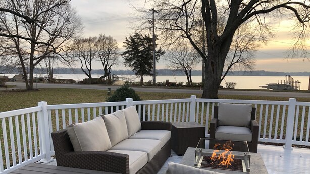 A deck with wicker furniture, a fire pit, and a view of a lake. - Powers Lake spacious retreat (Powers Lake)