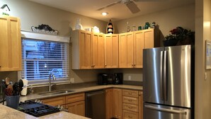 A modern kitchen with wooden cabinets, a stainless steel refrigerator, and a window with blinds. - Powers Lake spacious retreat (Powers Lake)