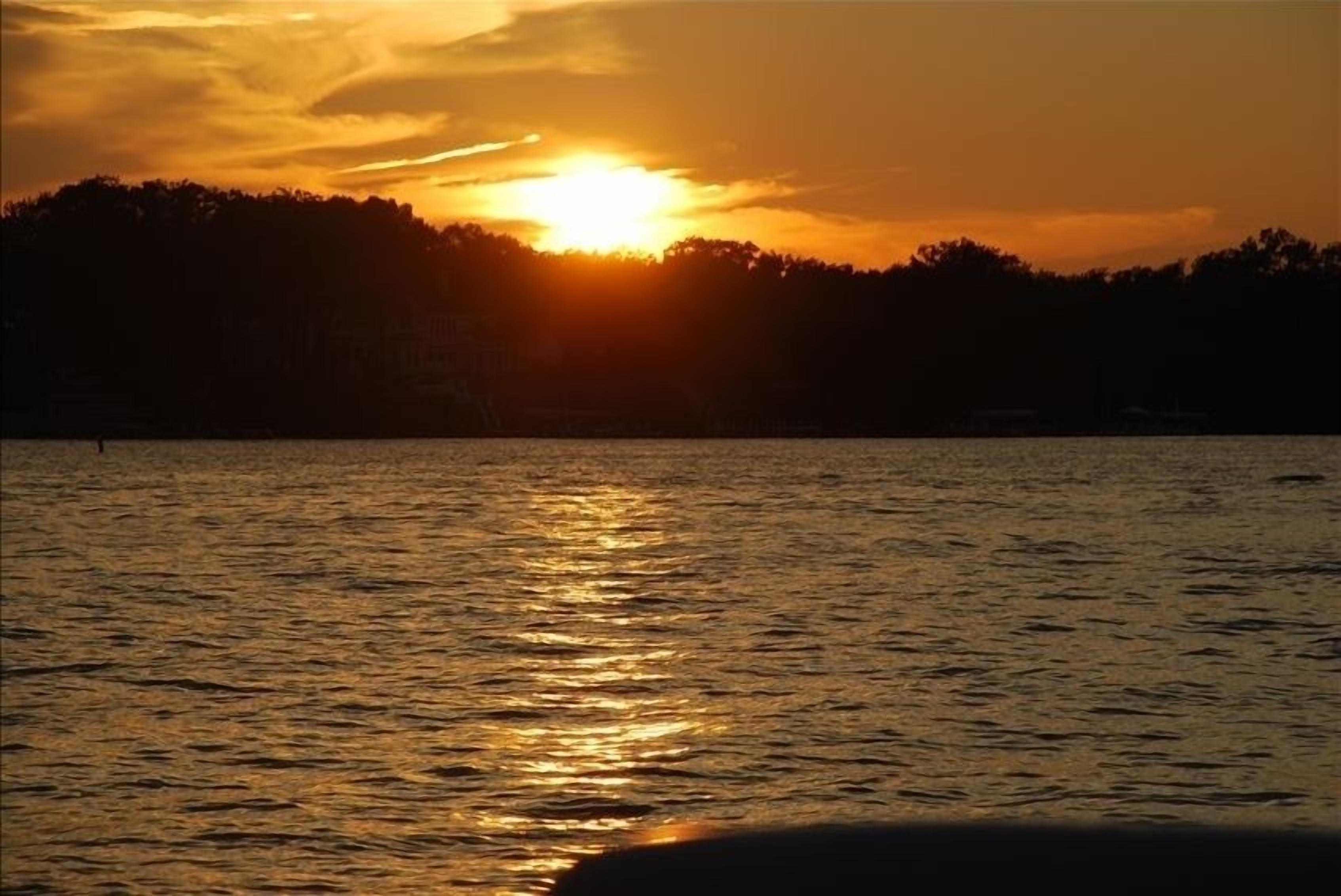 Un coucher de soleil sur une étendue d’eau, avec la silhouette d’arbres en arrière-plan.