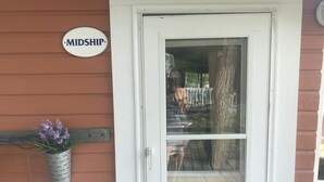 A house with a white door, a sign reading "MIDSHIP", and a small potted plant with purple flowers on the porch. - Snug Harbor Inn - Midship Cottage (Sturgeon Bay)