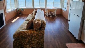 A cozy cabin with a wooden interior, a sofa, a dining table, and a view of the ocean through large windows. - Snug Harbor Inn - Midship Cottage (Sturgeon Bay)