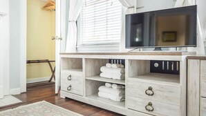 Une pièce avec un meuble TV en bois, un téléviseur à écran plat et une fenêtre équipée de stores.