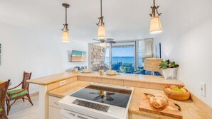A modern kitchen with a central island, a built-in stove, and pendant lighting. - Updated OceanFront Whale Watching - Kulakane 211 (Lahaina)