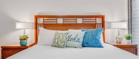A neatly made bed with a wooden headboard, multiple pillows, and bedside tables with lamps and small plants.