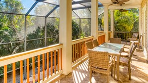A covered patio with wicker furniture and glass-top tables, surrounded by large windows offering views of tropical foliage. -  FREE golfcart and bicycles, Perfect location, 5 star reviews, beautiful home ! (captiva island)